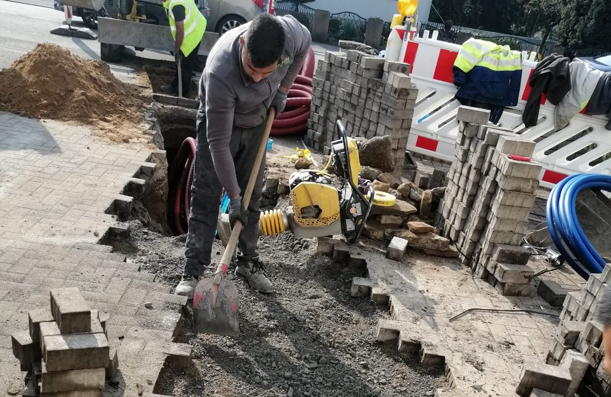 Straßenaufbruch mit ausgebautem Pflaster, ein Bauhelfer zieht den Untergrund mit der Schaufel ab