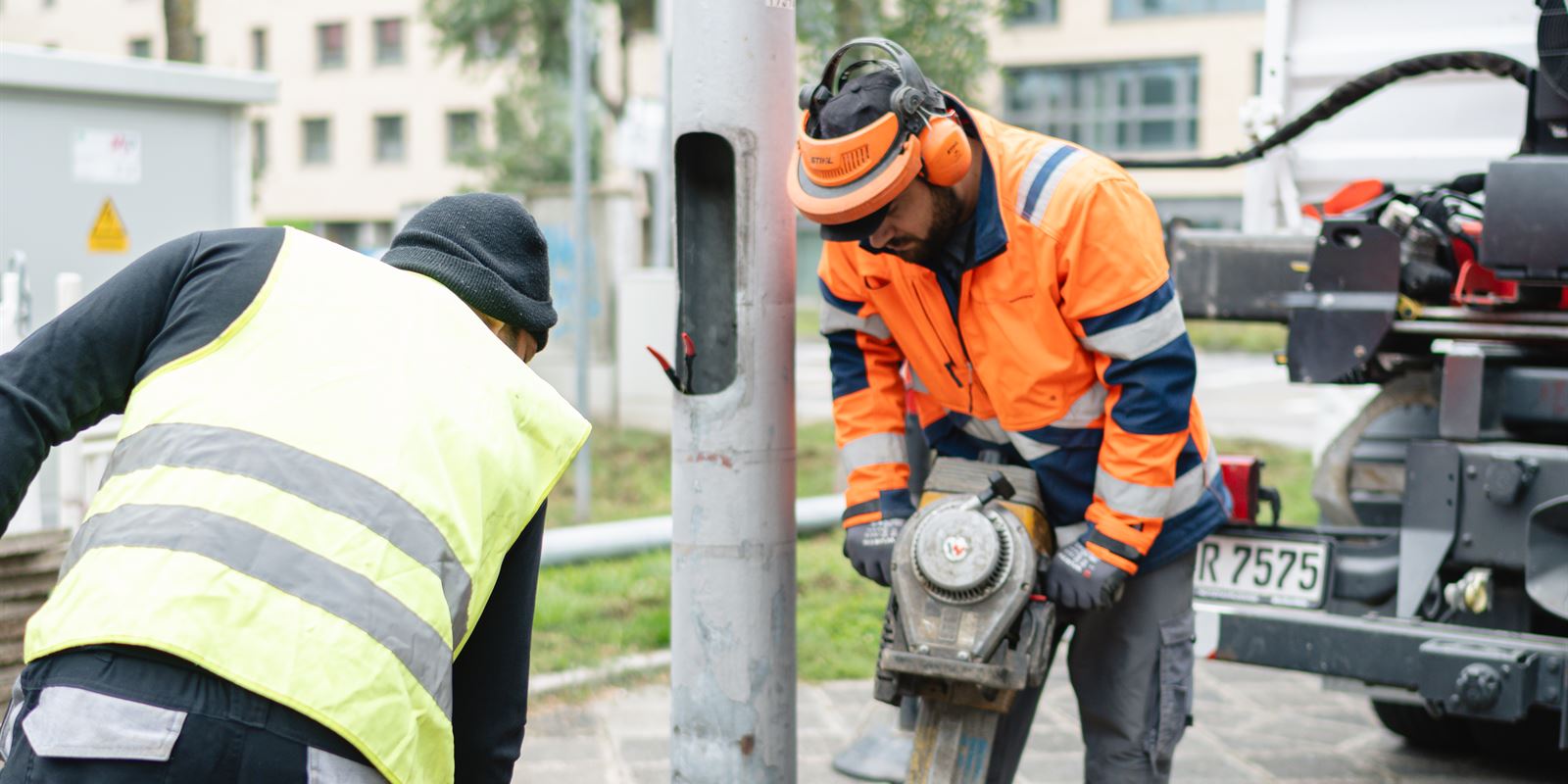 Zwei Mitarbeiter von Seith Energietechnik brechen mit Presslufthammer und Schaufel eine Fläche an einem Mast auf